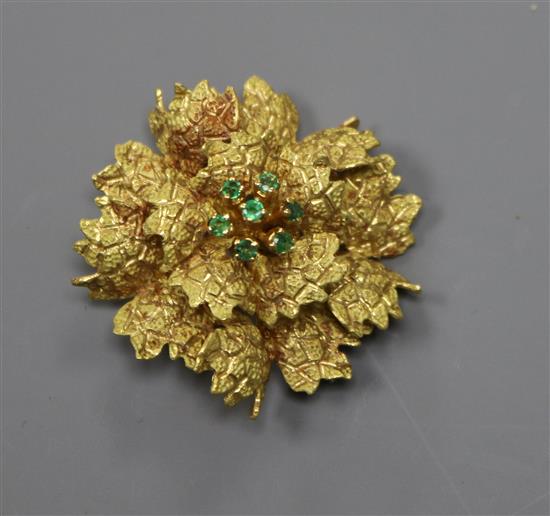 A continental 18k yellow metal and emerald set flower head brooch, 35mm.